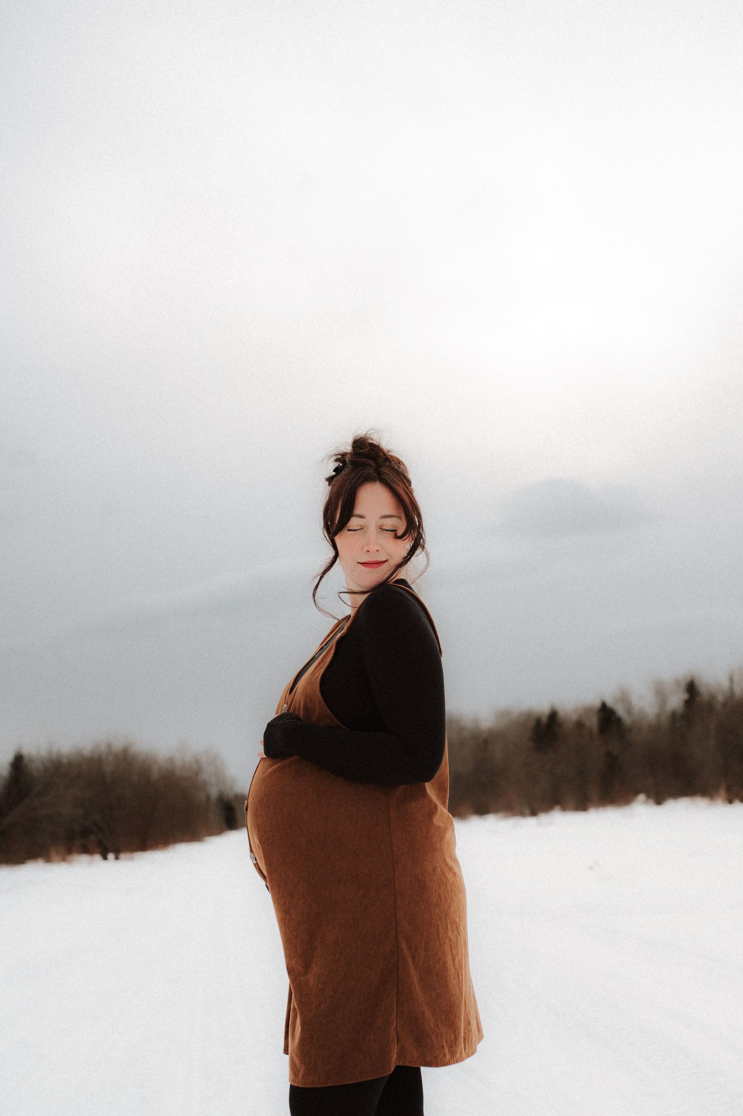 A person wrapped in a brown blanket stands in a snowy winter landscape against an overcast sky.