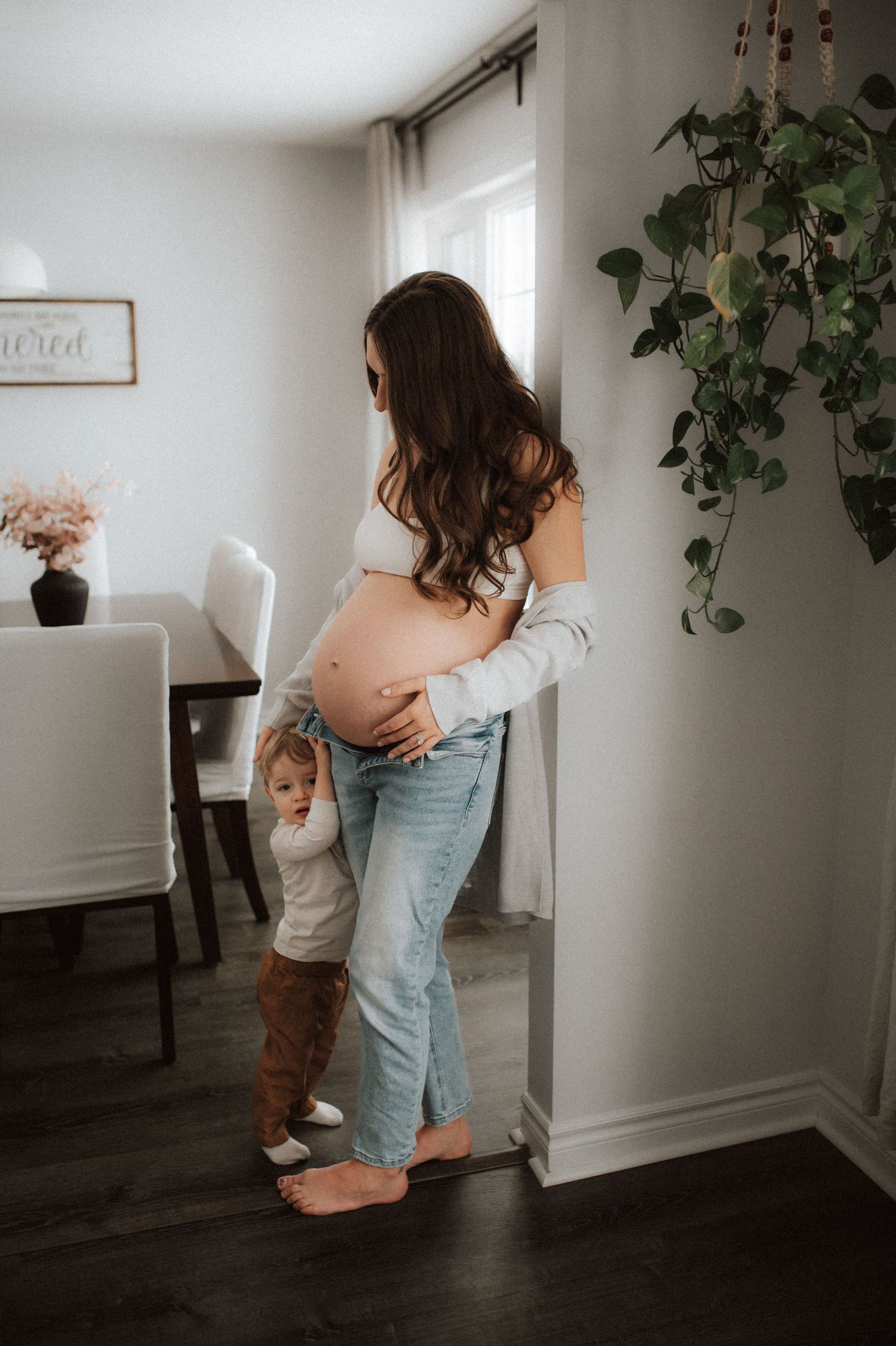 A parent and toddler dancing in a sunlit living room with houseplants and hardwood floors.