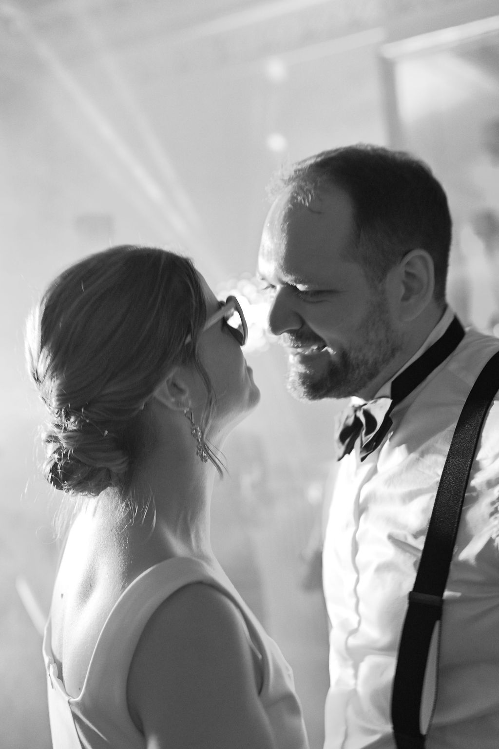 Black and white romantic wedding moment with couple gazing at each other, bride in white dress and groom in suspenders.