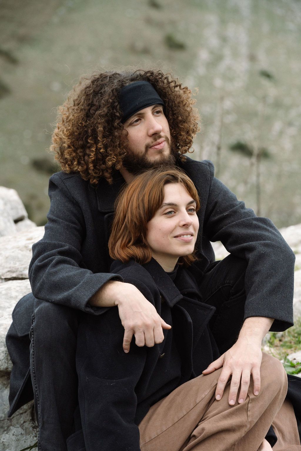 Two people wearing black coats sit together on a stone surface in a series of candid outdoor moments.