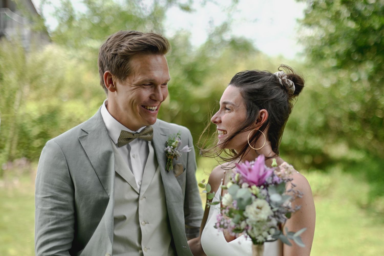 A couple in wedding attire shares a tender moment outdoors in a natural garden setting.