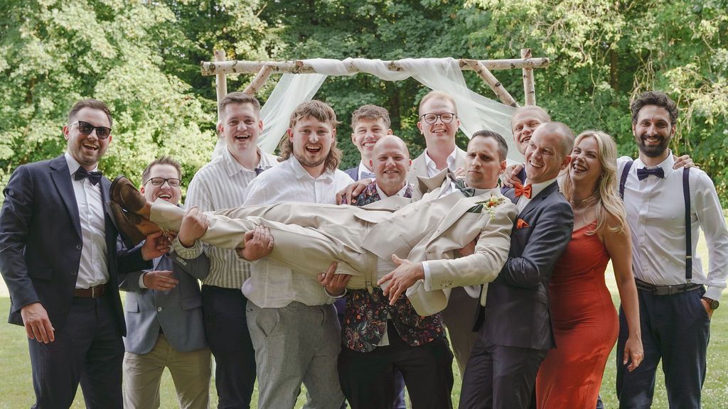 Wedding party groomsmen lined up outdoors holding beer bottles in a celebratory toast pose.