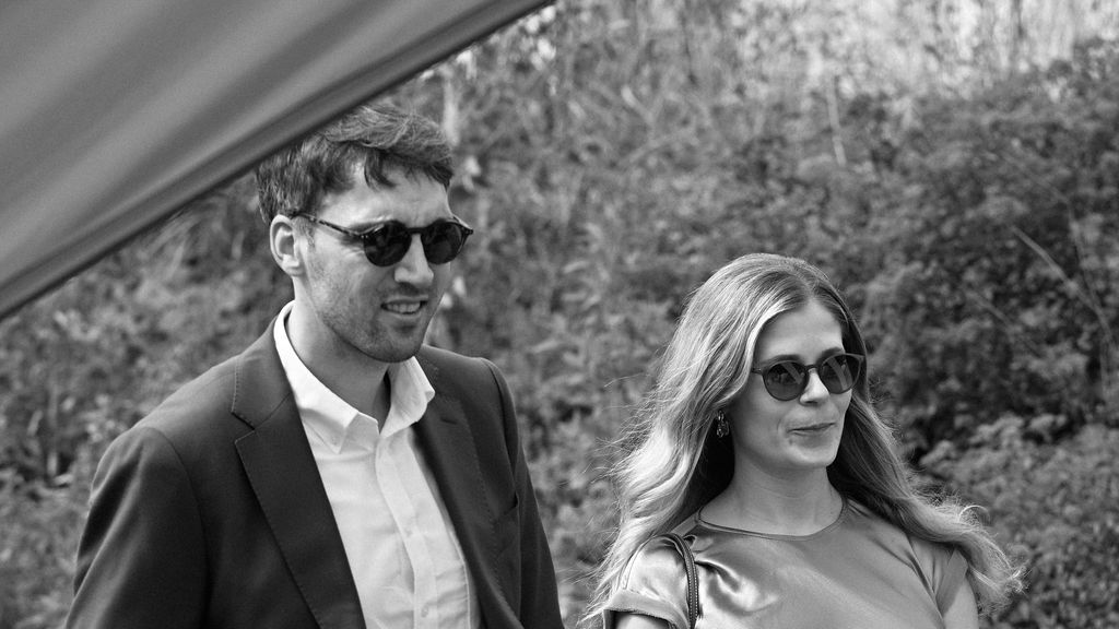 A couple wearing sunglasses walks together outdoors in a black and white photograph.