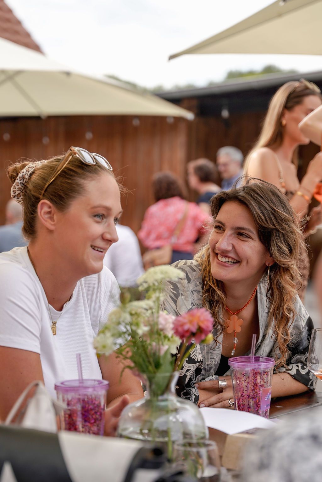 People enjoying a casual outdoor dining experience with drinks and flowers on the table at a social gathering.