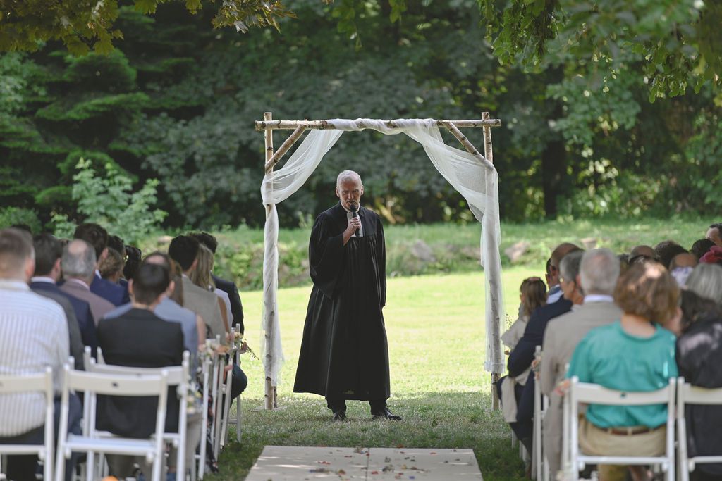 An outdoor wedding ceremony setup with white chairs and an officiant standing under a simple white arch.