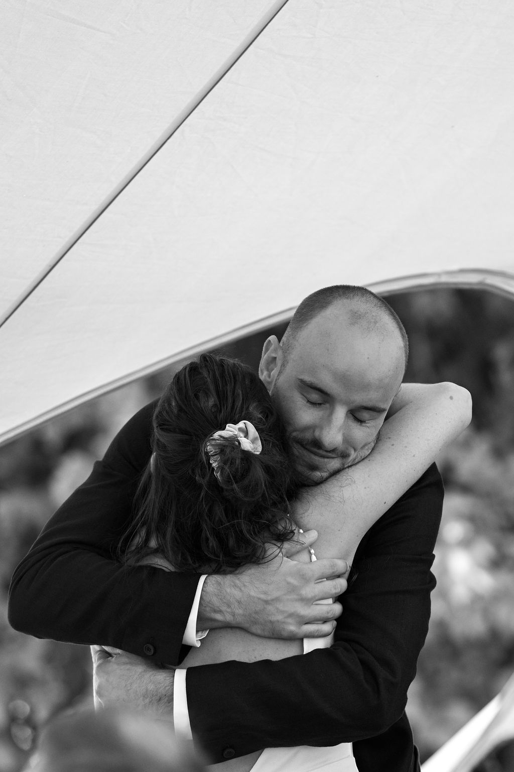 A black and white photograph of a tender embrace between two people during what appears to be a wedding moment.