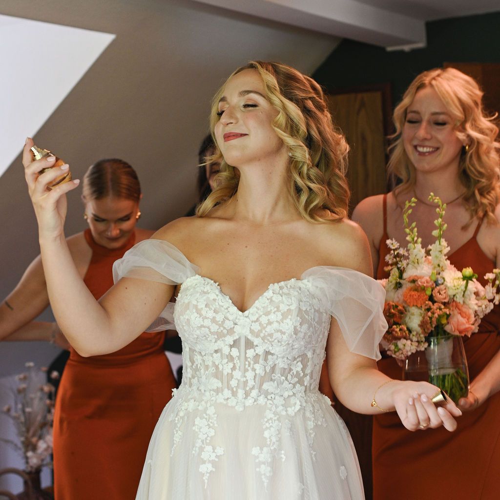 A bride in a white lace wedding dress dances joyfully with bridesmaids in rust-colored dresses.