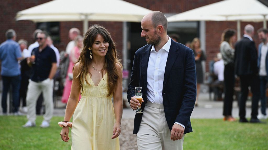 People enjoying a garden party with white umbrellas and formal attire at an outdoor event.