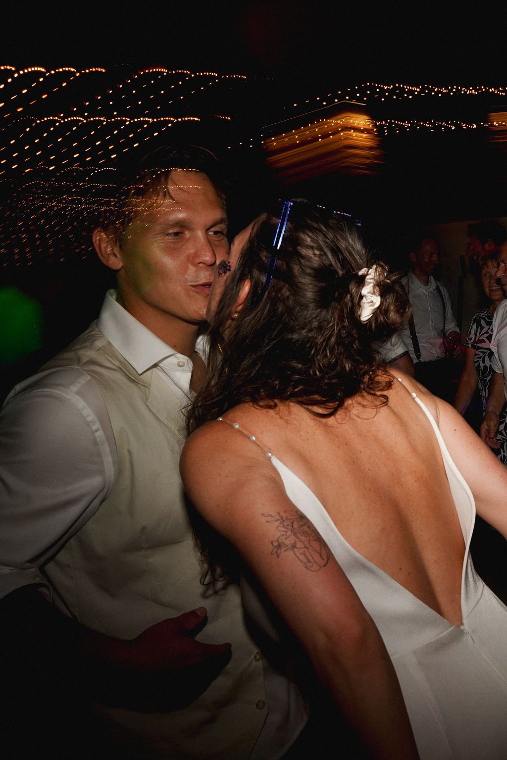Couples dancing together at a dimly lit reception with string lights overhead creating a romantic atmosphere.