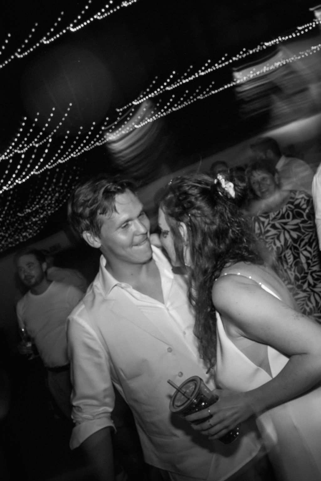 Couples dance together at a nightclub with glittering lights visible overhead in a black and white photograph.