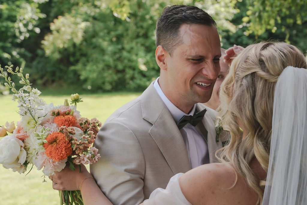 A couple embraces during their wedding ceremony in a lush outdoor garden setting.