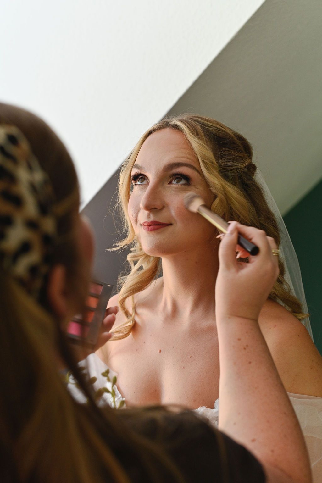 Makeup artist applies cosmetics to a bride's face during wedding day preparations.