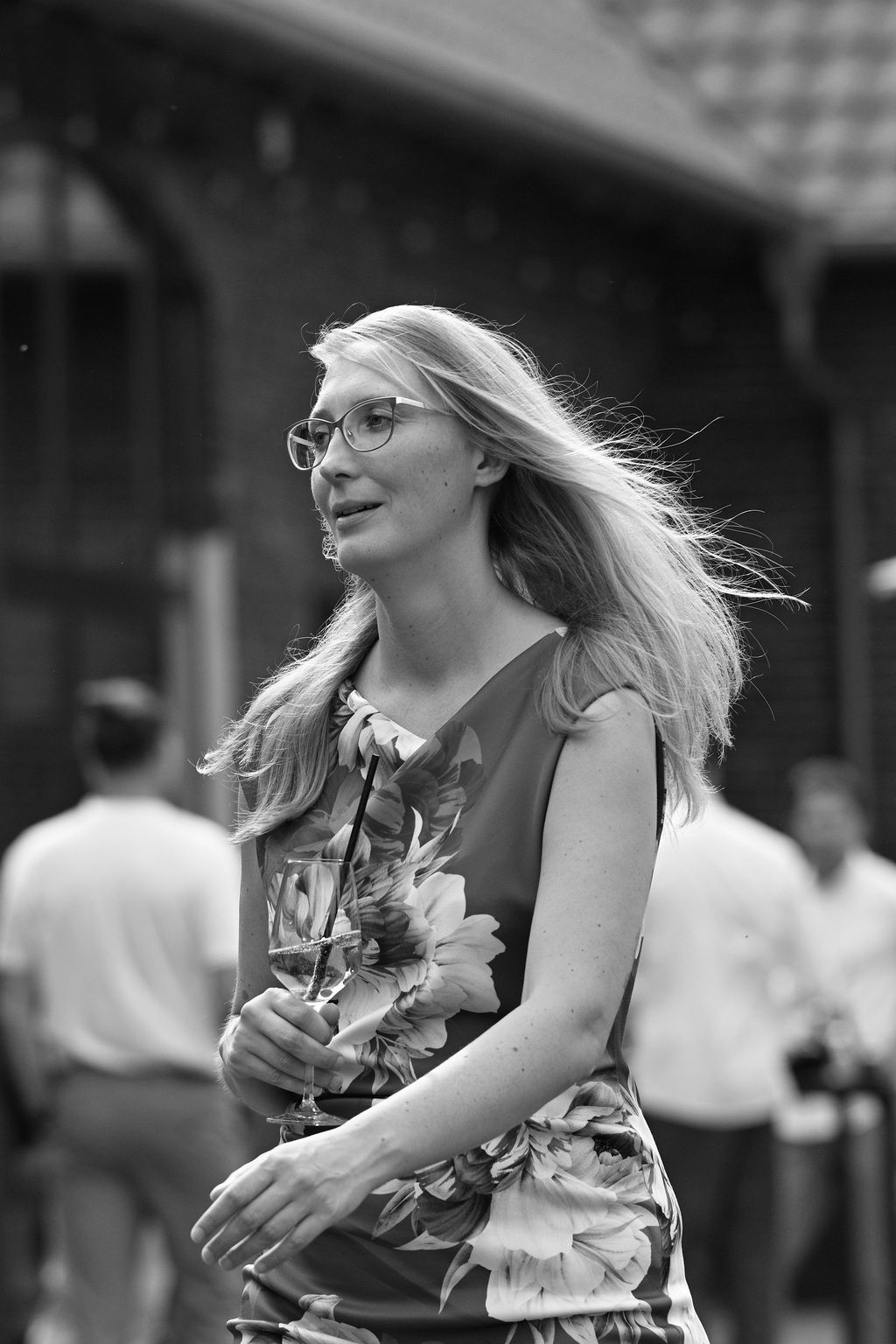 A black and white portrait of someone with glasses and flowing hair holding flowers while walking outdoors.