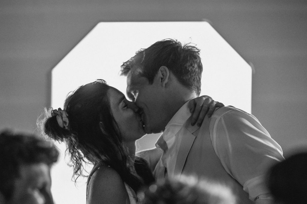 A romantic black and white photograph captures a couple sharing a tender kiss during what appears to be their wedding day.