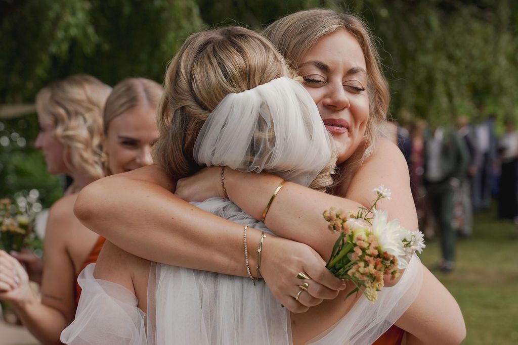 People embrace in a series of emotional hugs during an outdoor wedding celebration in a garden setting.