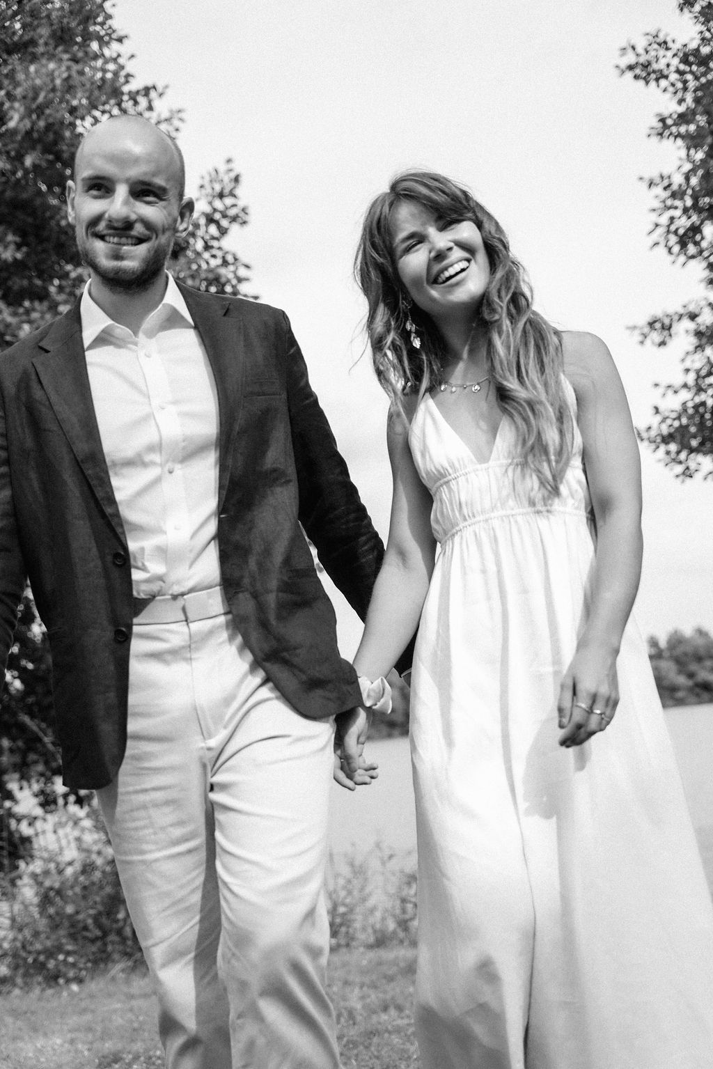 A happy couple walks hand in hand through a garden setting, with the bride in white and groom in a dark suit.