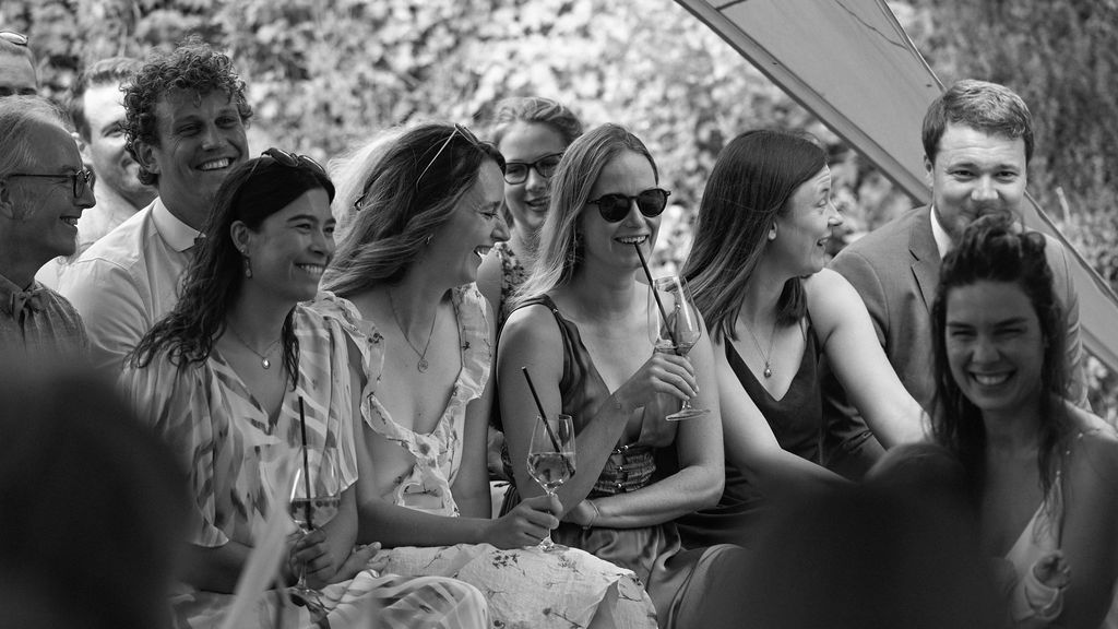 A black and white candid photograph shows a group of people gathered outdoors enjoying a casual social gathering.