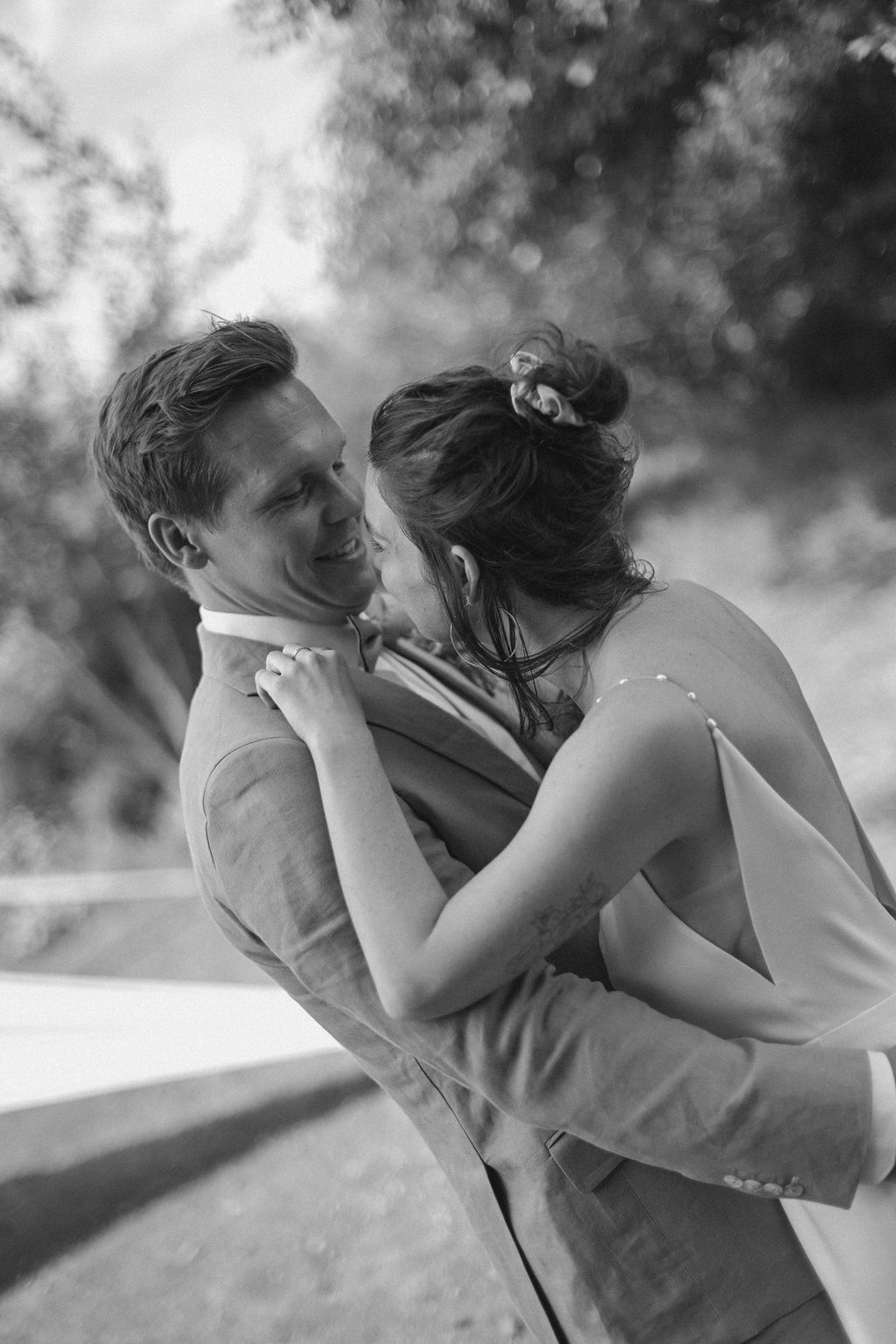 A romantic black and white wedding photo captures an intimate moment between a couple in formal attire outdoors.