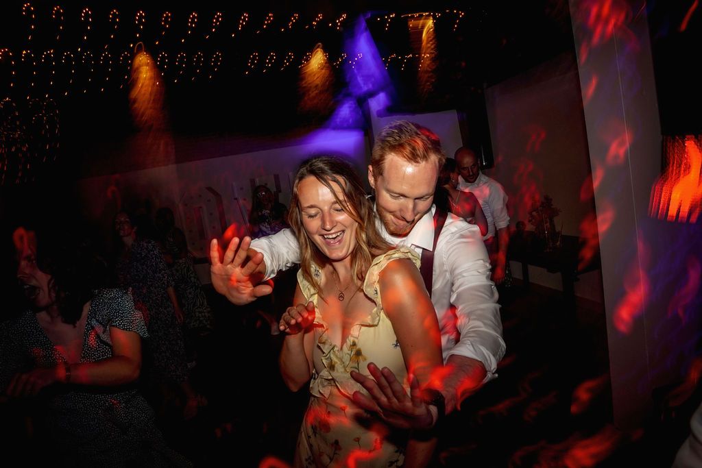 Couple dancing together under colorful nightclub lighting with orange and purple hues creating a festive atmosphere.