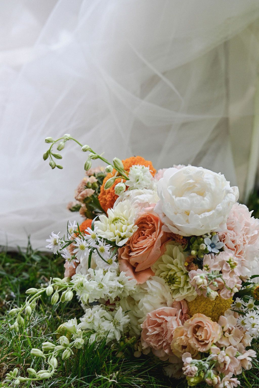 A romantic floral arrangement featuring white peonies, peach roses, and delicate greenery against a soft tulle backdrop.
