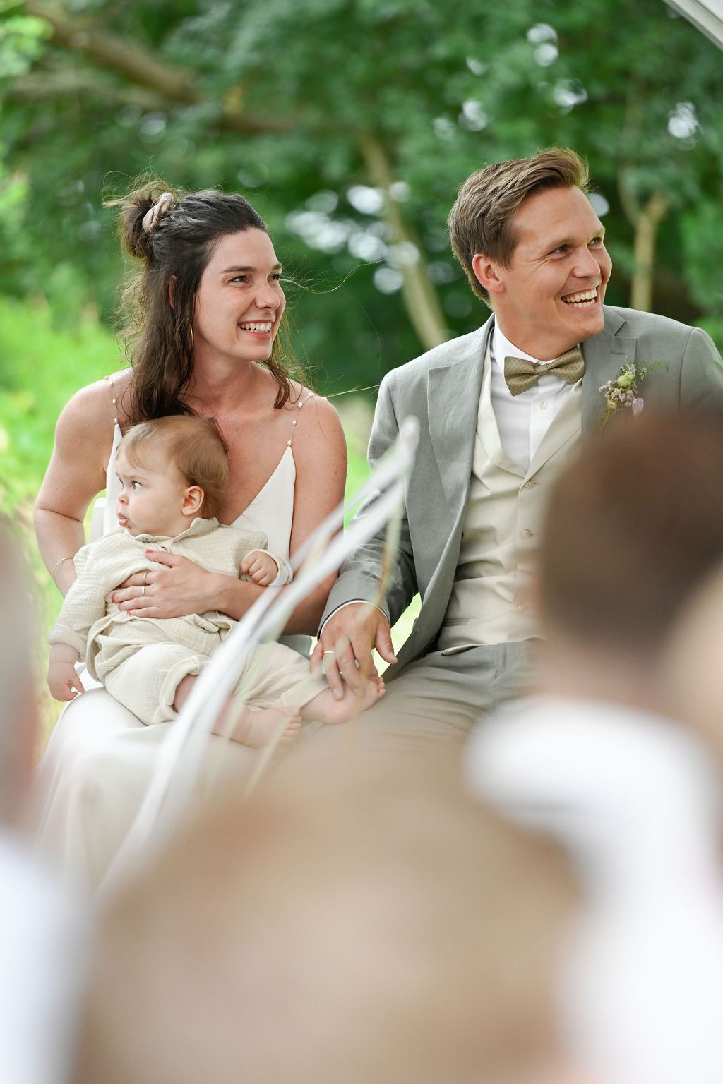 Wedding guests smile and celebrate during an outdoor summer reception in a lush green garden setting.