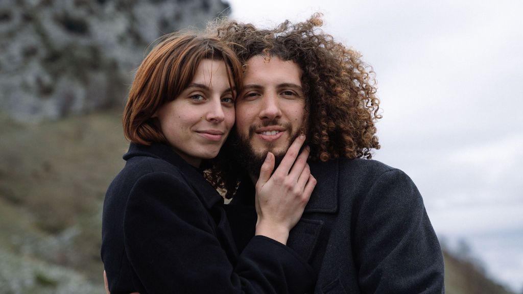 A couple shares an intimate moment while standing outdoors against a cloudy sky.
