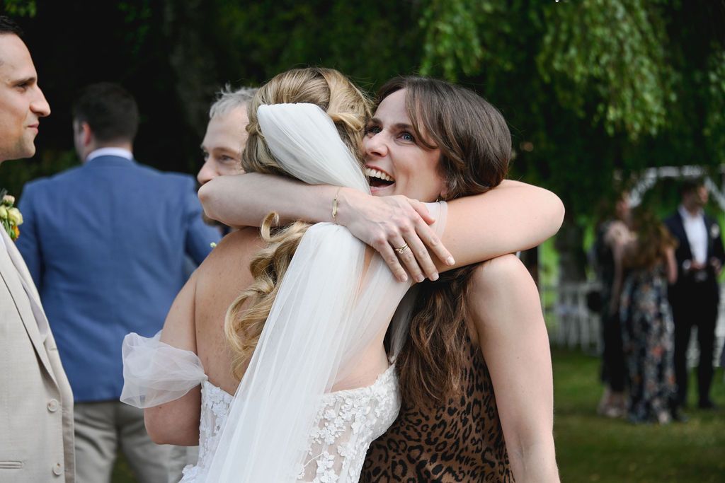 Wedding guests embrace and celebrate during an outdoor reception in a lush garden setting.