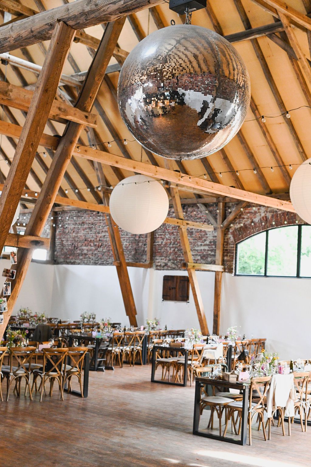Large rustic event venue with exposed wooden beams, disco ball, and tables set up for a reception or celebration.