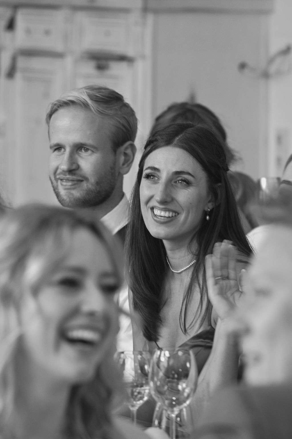 A group of people laughing and socializing at a dinner party with wine glasses on the table.