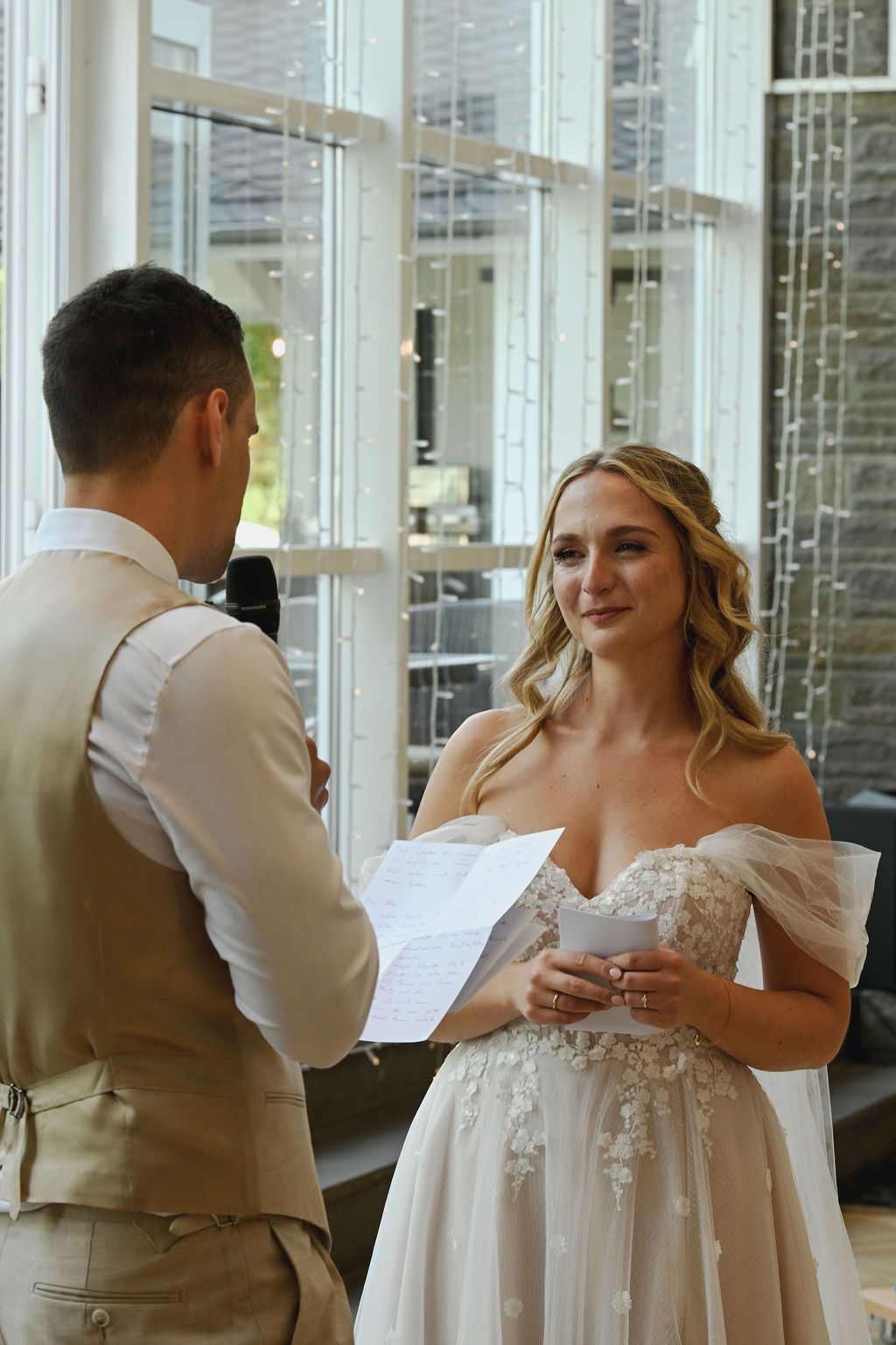 A couple in wedding attire share a tender first look moment in a bright, window-lined venue.