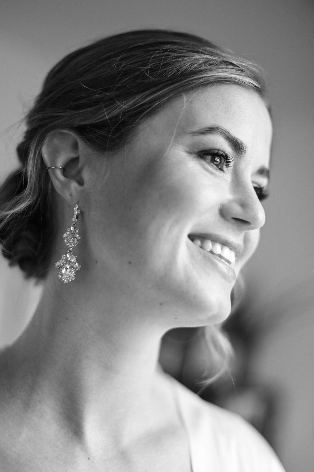 Black and white close-up profile portraits showing elegant crystal earrings and soft smiles in a bridal photoshoot.