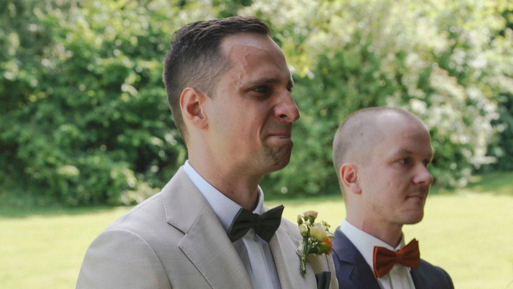 A couple shares a tender moment outdoors in a garden setting during a wedding celebration.