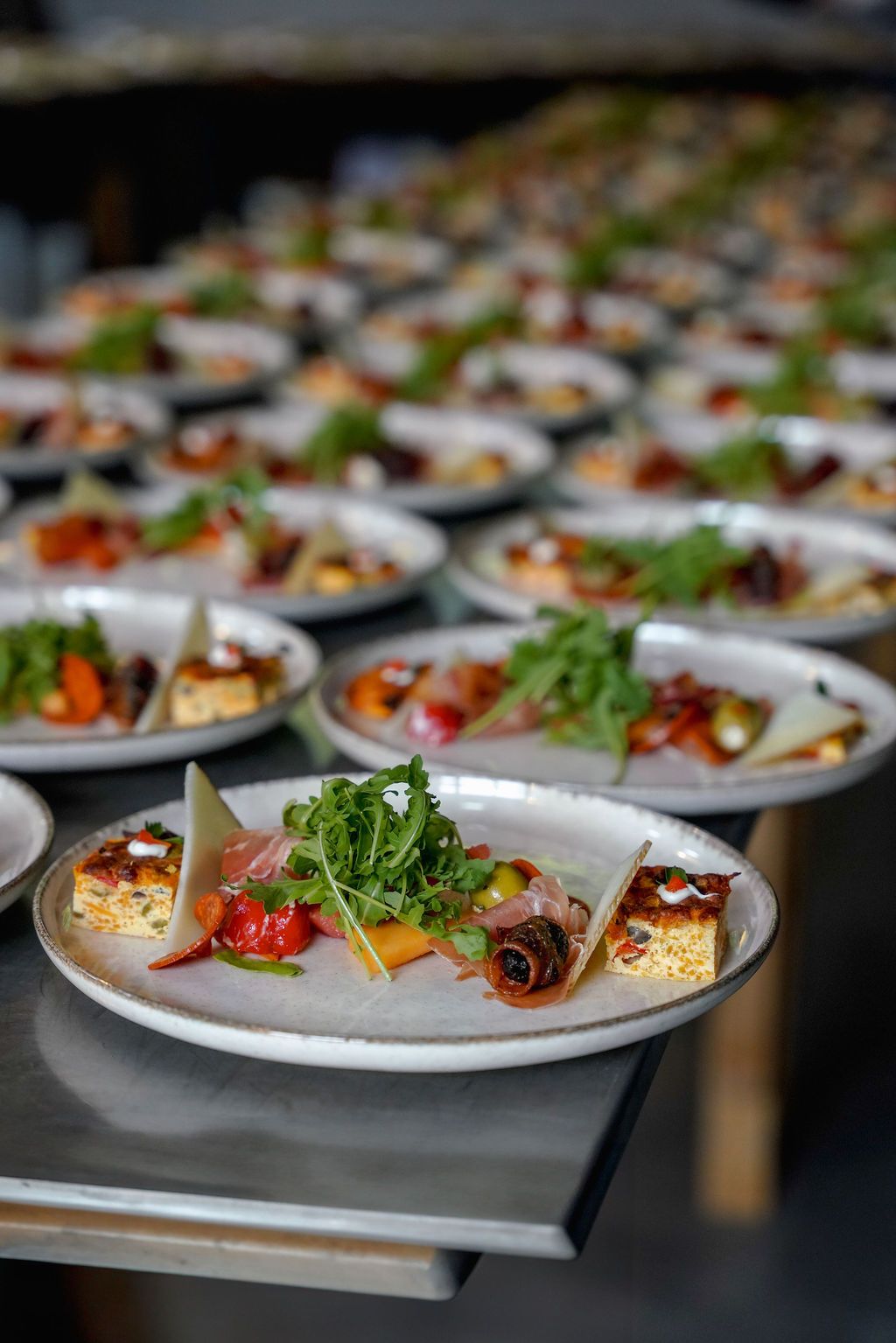 Rows of elegantly plated appetizers on white dishes featuring colorful garnishes and sauces.
