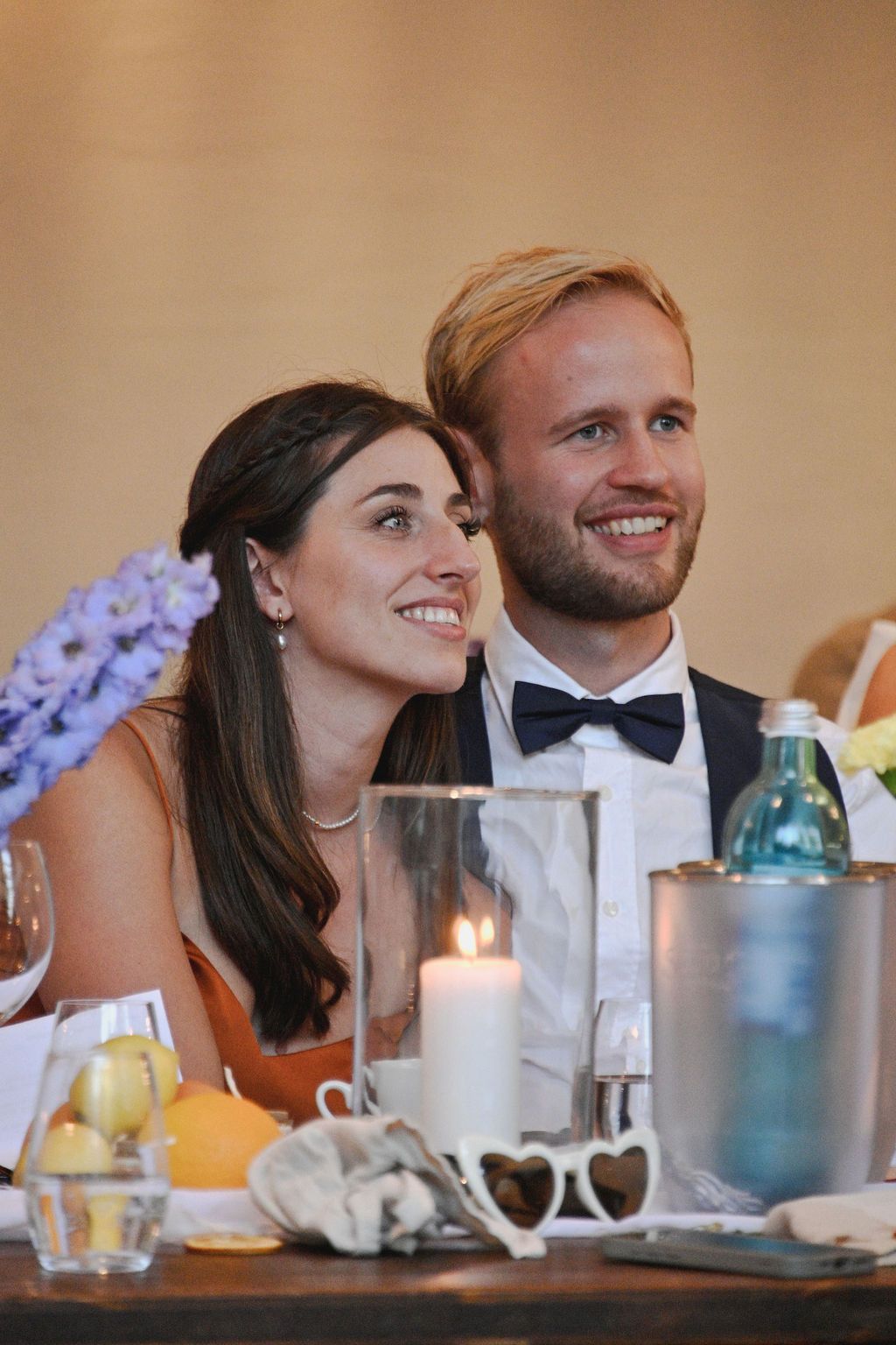 A couple shares a romantic moment at a wedding reception table decorated with candles and flowers.