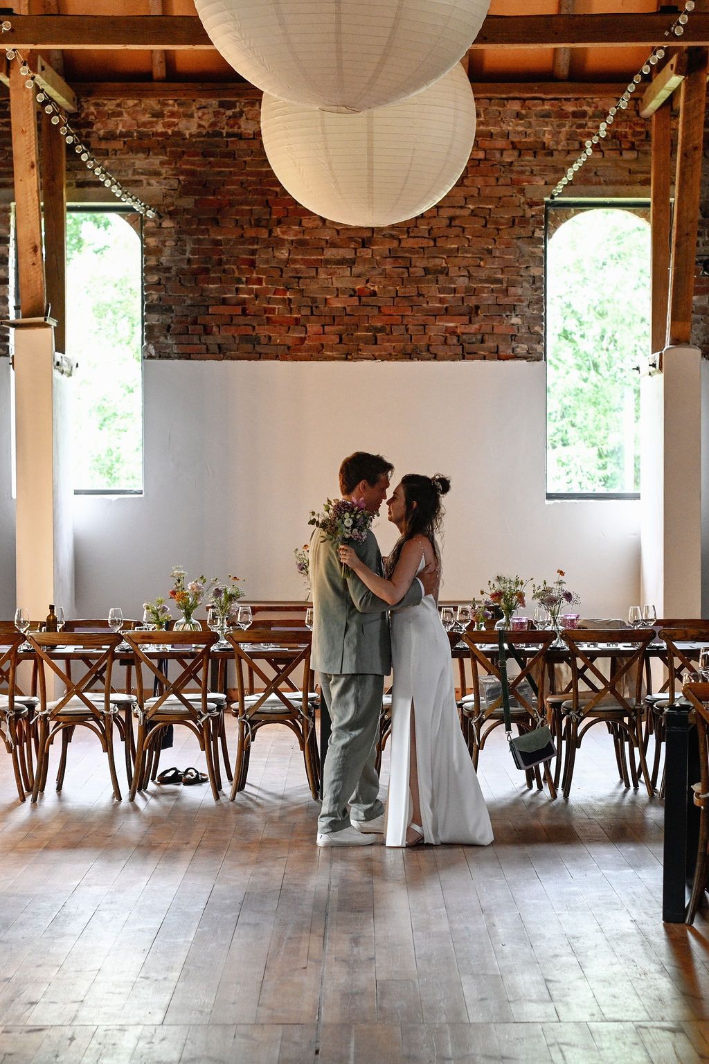 A romantic couple shares a tender moment in a rustic venue with exposed brick walls and paper lanterns overhead.