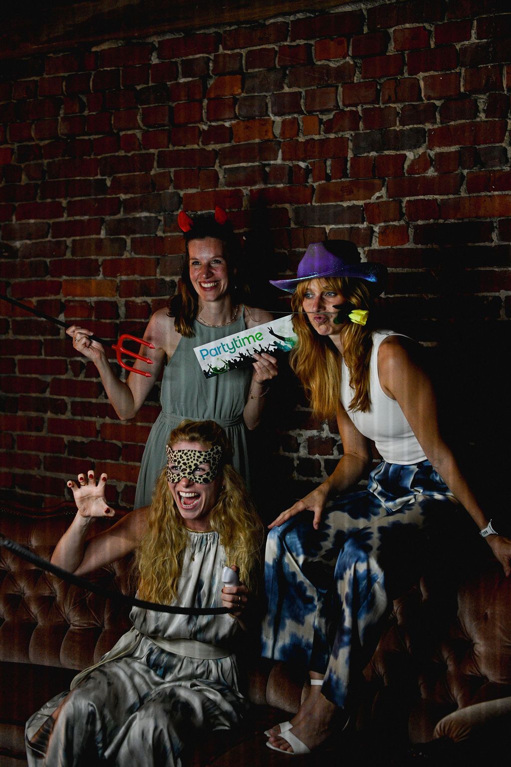 People enjoying a party with props and costumes against a brick wall backdrop in dimly lit ambiance.