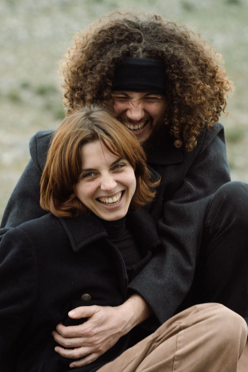 Two people in dark coats sharing a joyful laugh together while embracing outdoors.