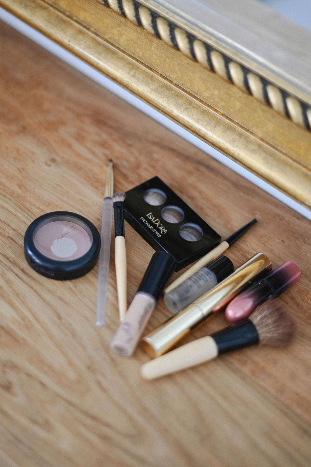 Makeup brushes and cosmetic products arranged on a wooden surface with gold trim molding in the background.