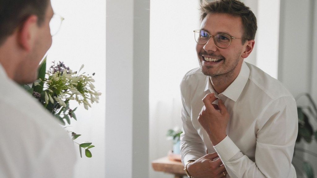 Professional wearing a white shirt and glasses smiles during a business meeting in a bright office setting.