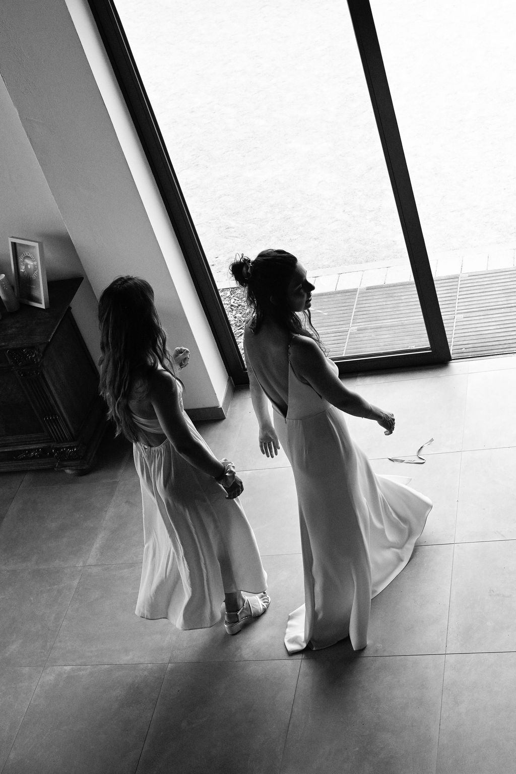 Two dancers in flowing white dresses perform an elegant dance sequence in a studio.