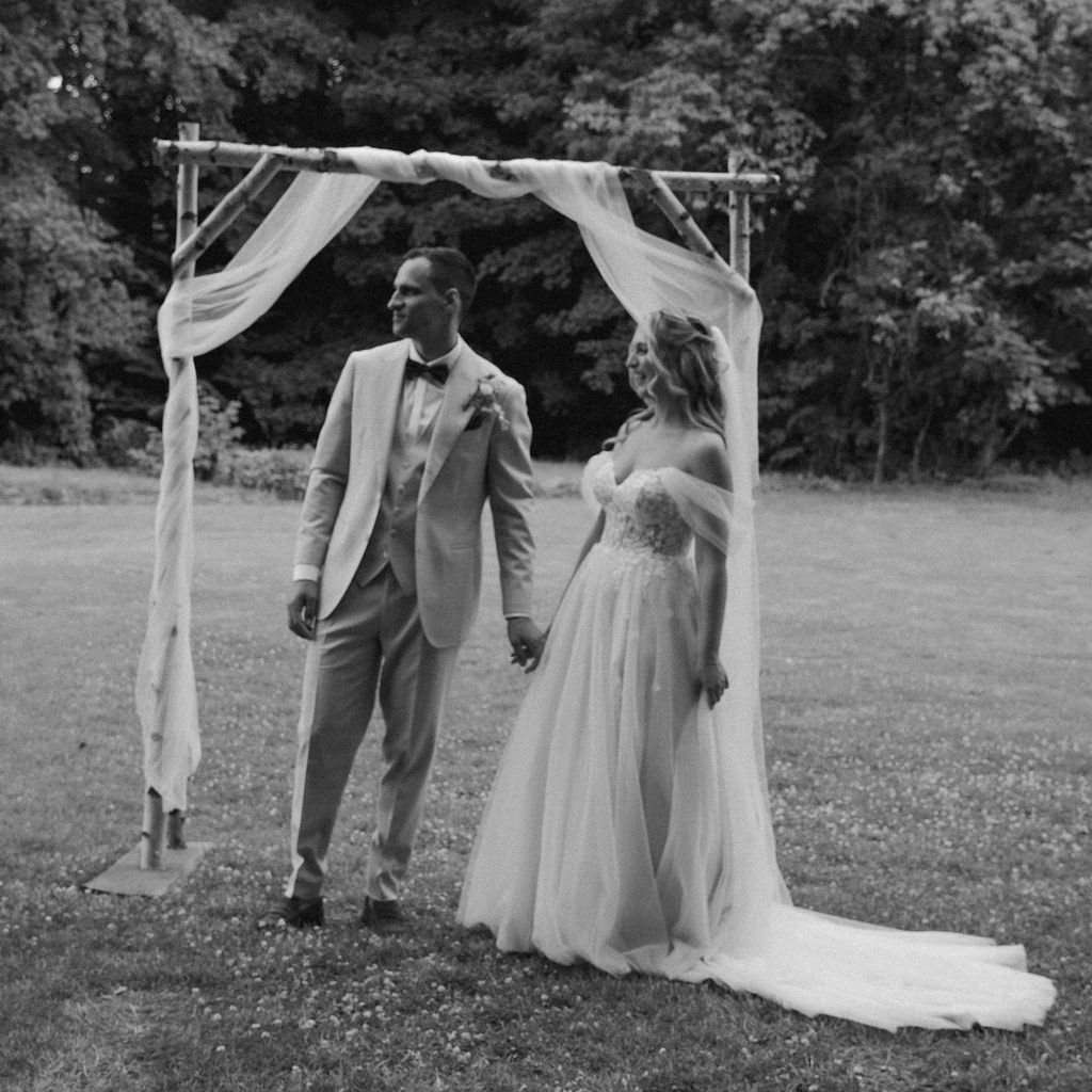 Wedding party members walk across a grassy field in elegant formal attire during an outdoor celebration.