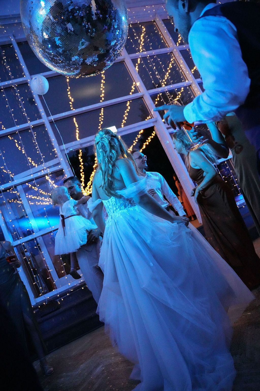 A person in a flowing white gown dances under twinkling fairy lights at an evening celebration.