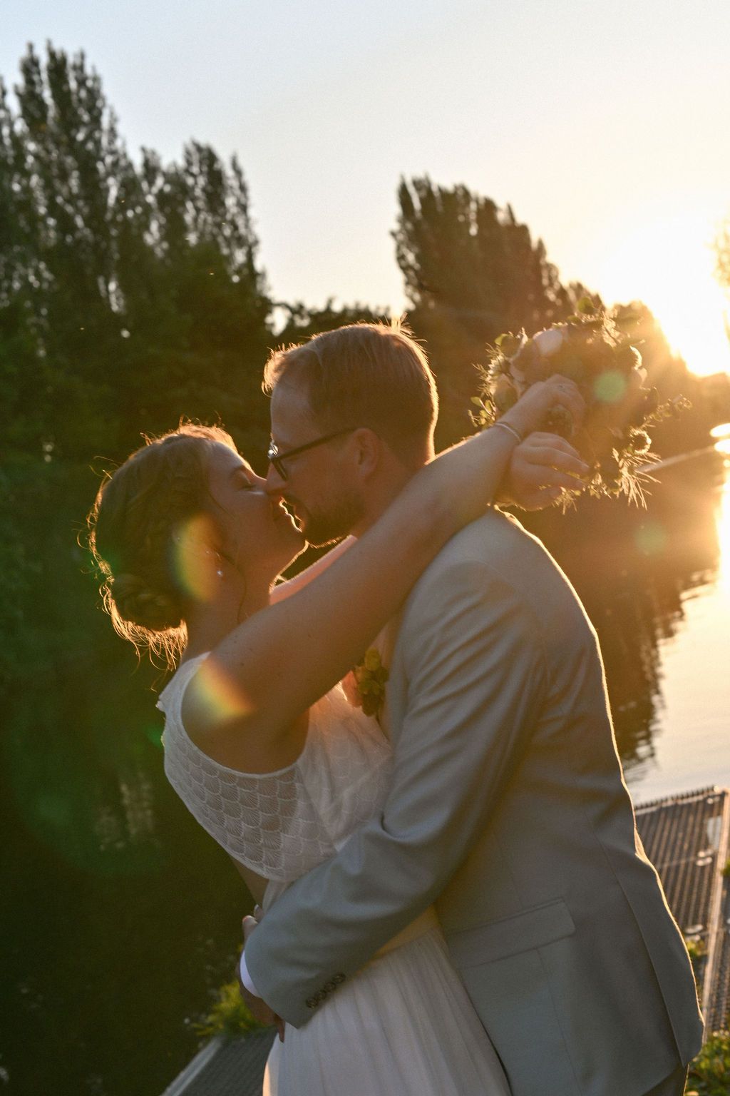 Silhouetted couple embracing during golden hour sunset with trees in background.