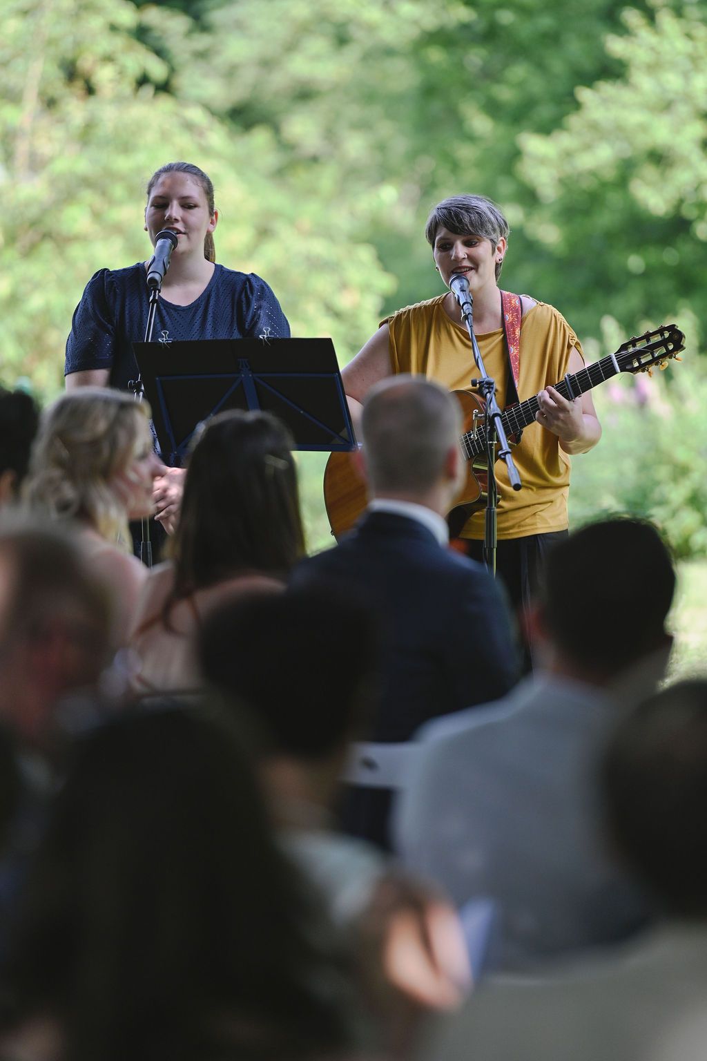 Musicians perform at an outdoor concert venue with a crowd of spectators watching in the foreground.