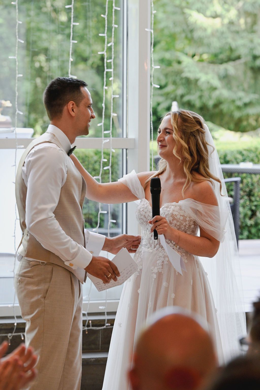 A couple shares their first dance at a wedding reception in a bright venue with glass walls.