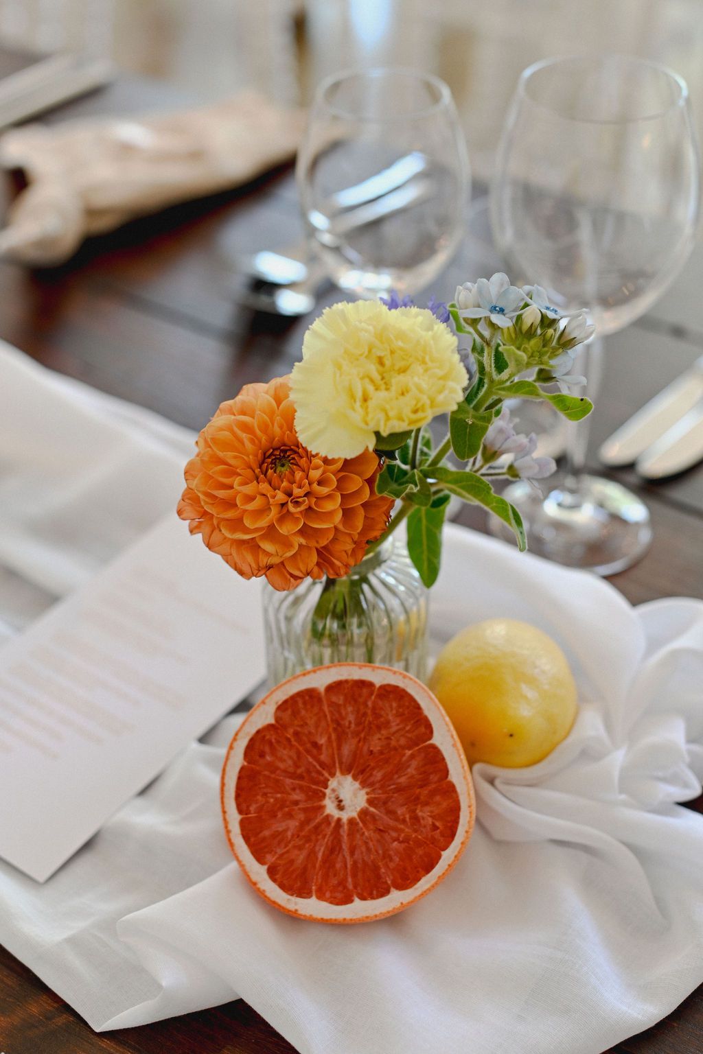 Elegant table setting with grapefruit slices and orange flowers in small vases arranged in a sequence of four photos.