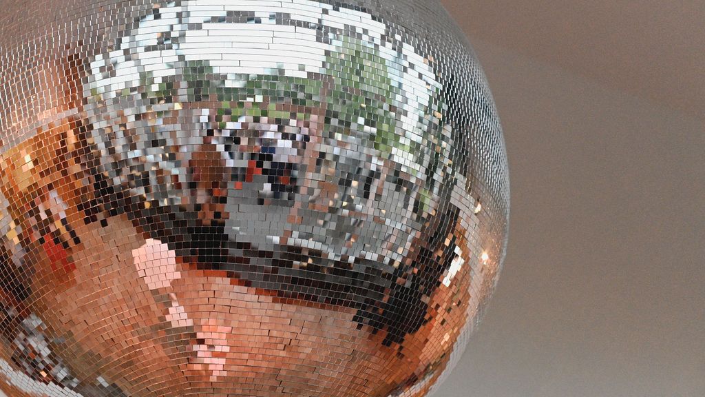 A large mirrored disco ball reflects light and people in a room creating a sparkling party atmosphere.