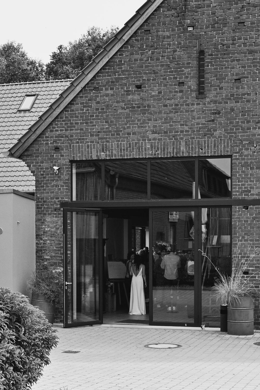 Black and white view of modern brick building entrance with glass doors and covered porch area.