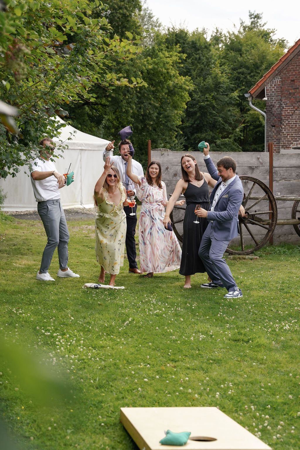 A group of wedding guests playing cornhole on a grassy lawn during an outdoor celebration.