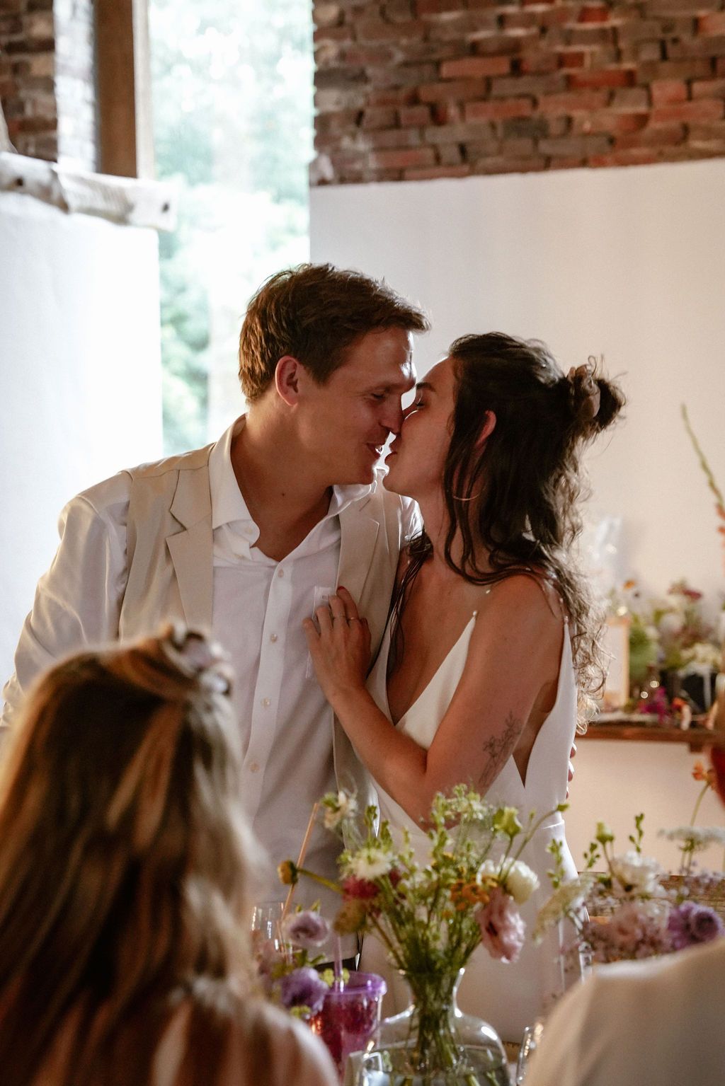 A romantic moment shared between a couple during a rustic indoor wedding reception with floral decorations.